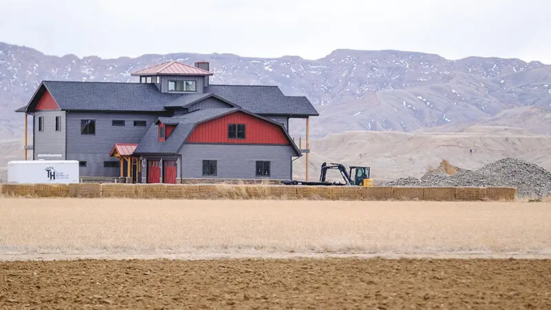 Two-story modern farmhouse-style home with red and gray siding set against Wyoming mountains